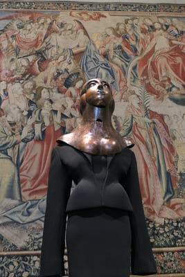 bronze metal headpiece and black skirt suit on mannequin in front of tapestry